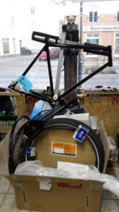 Fahrradrahmen am Montageständer, davor ein großer Karton übervoll mit Fahrradteile
